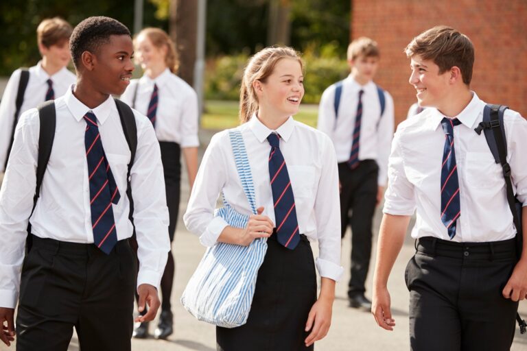 Studenti in uniforme scolastica inglese chiacchierano uscendo dalla scuola di mattoni rossi