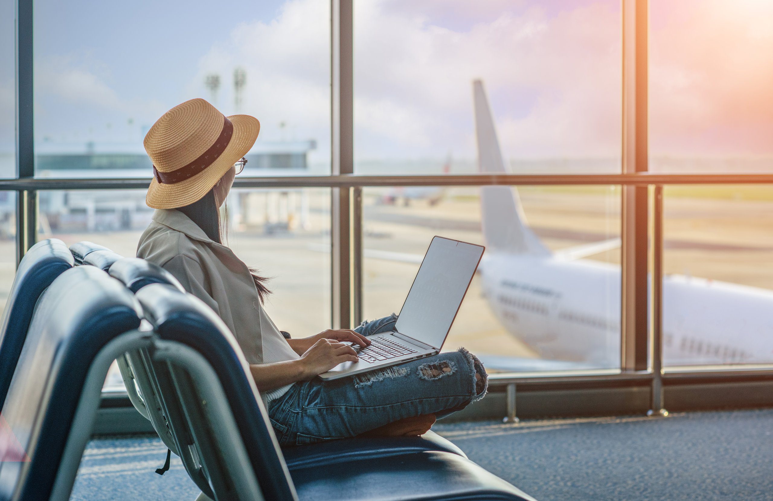 Una ragazza in aeroporto con il portatile davanti alle vetrate, un aereo sulla pista