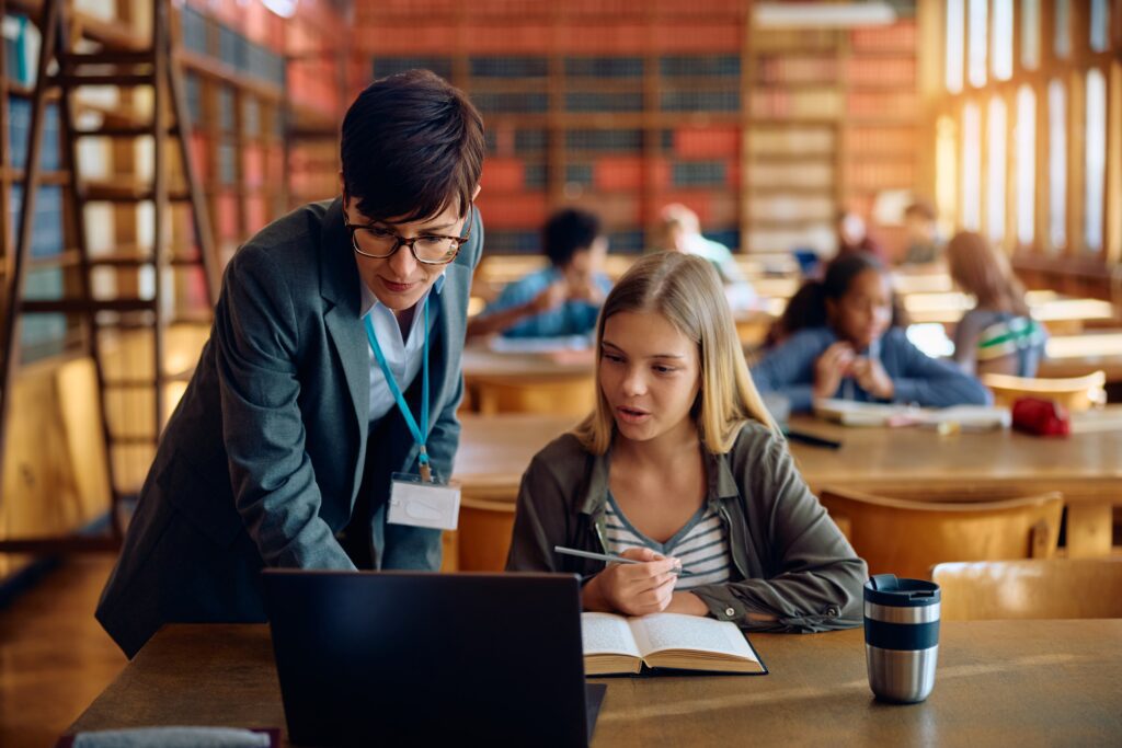 Un'insegnante affianca una studentessa al laptop nella biblioteca della scuola