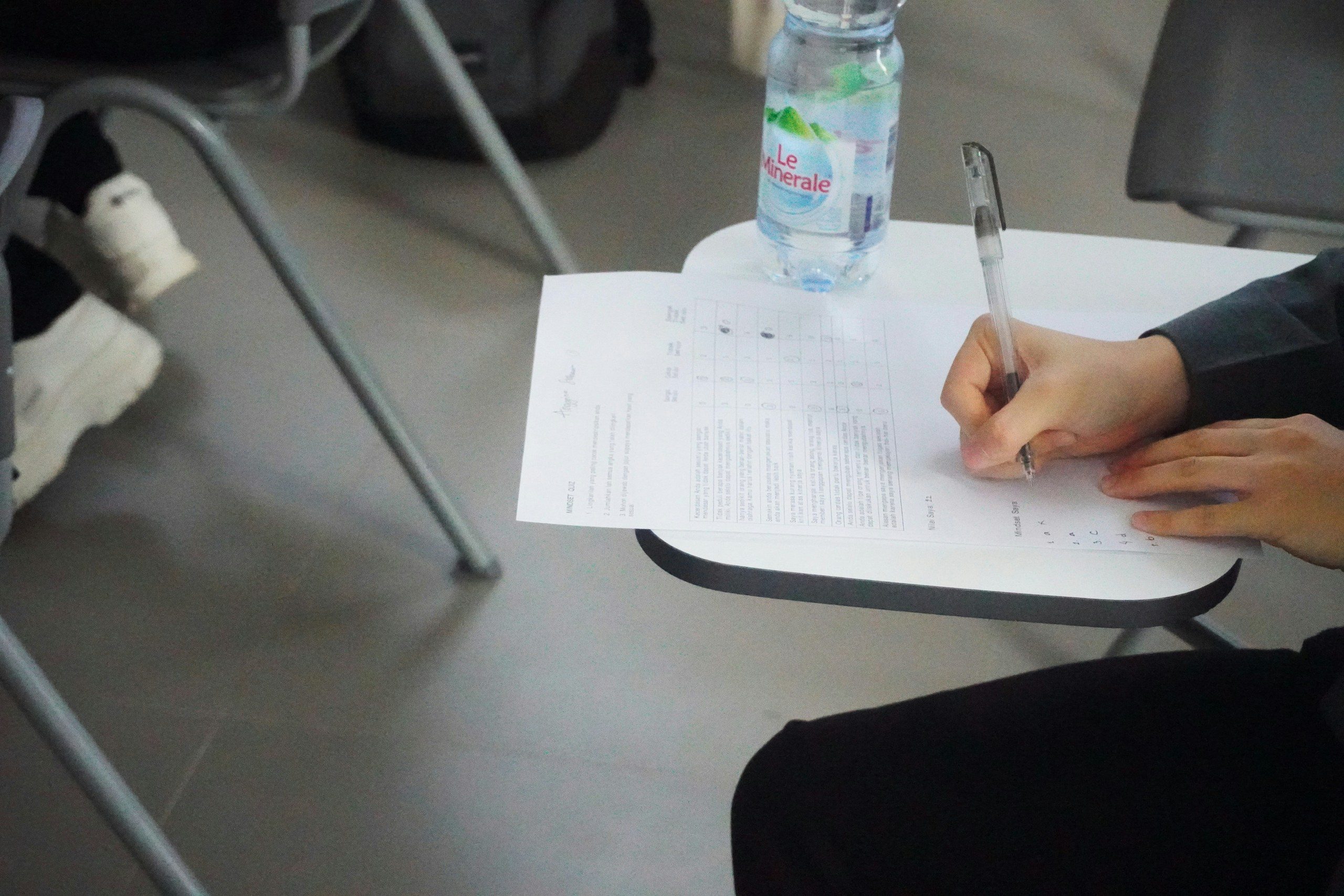 Mano di uno studente che compila il foglio risposte di un test, seduto al banco