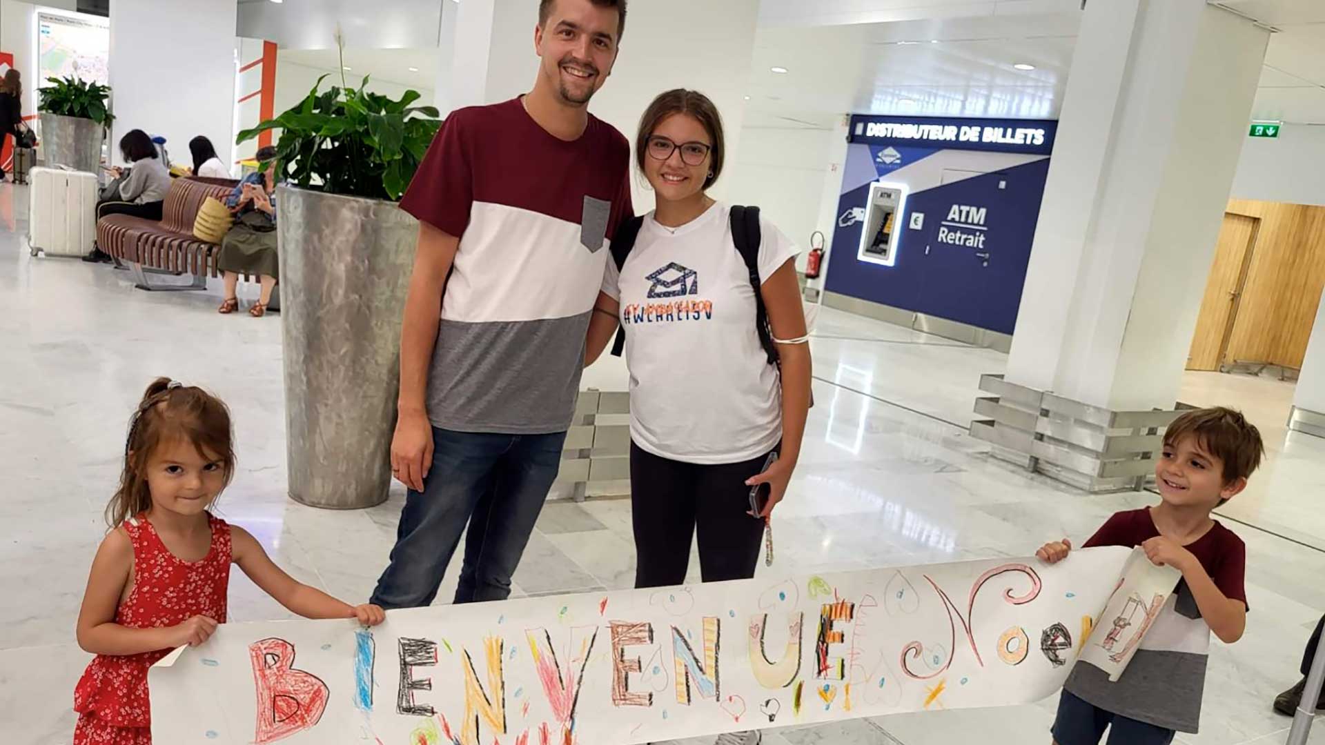 Famiglia ospitante accoglie uno studente con un cartello di benvenuto